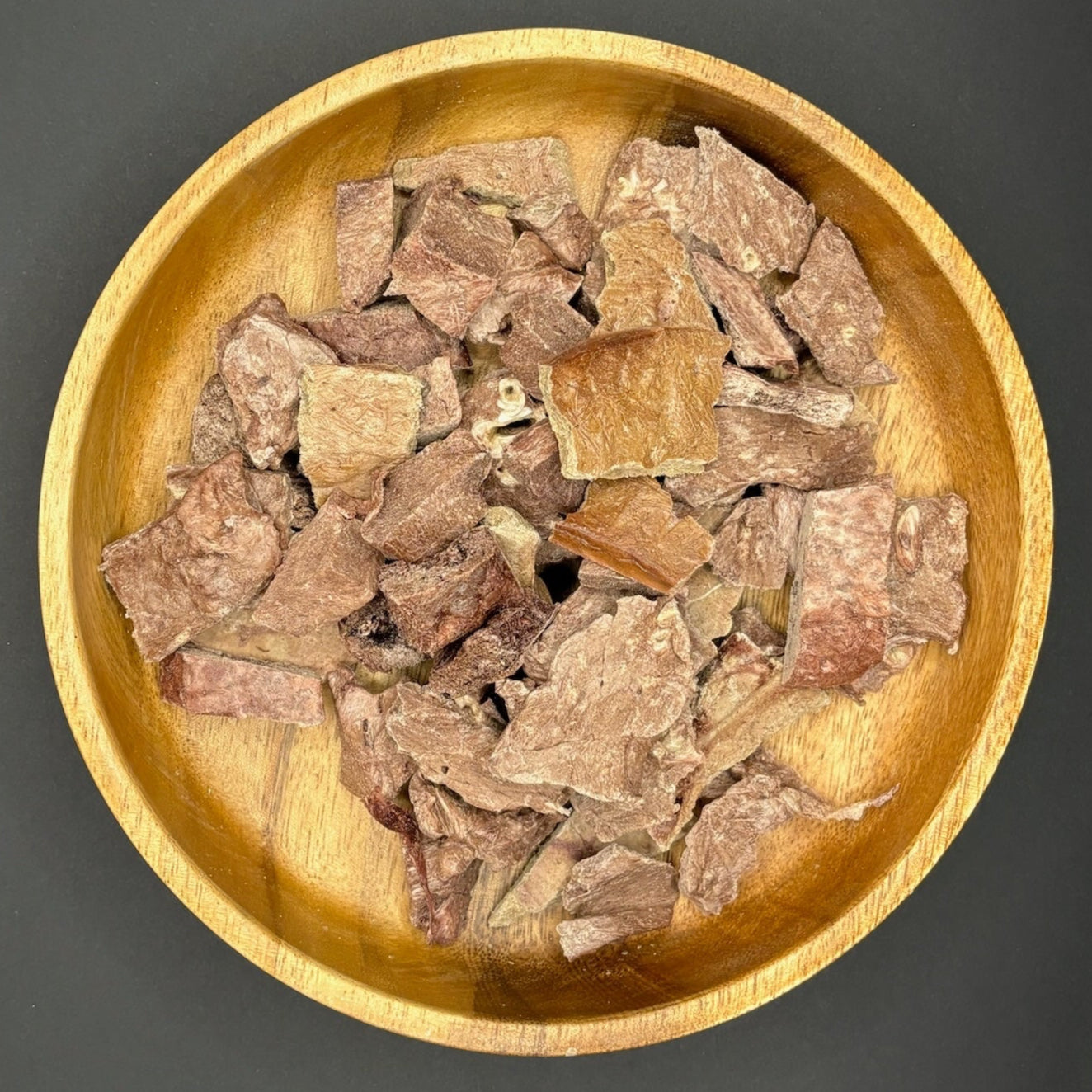 Close up of Carnevore Mountain Freeze Dried Beef Trail Mix Dog and Cat Treats in a brown wooden bowl with a gray background. 